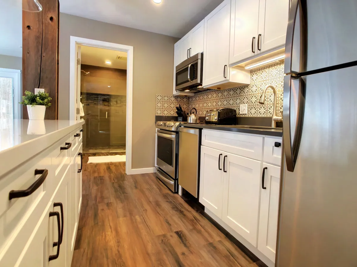 A modern, inviting kitchen with stainless steel appliances, white cabinetry, decorative backsplash, and wooden flooring. The setup is perfect for meal prep, socializing, and gathering before or after special events.
