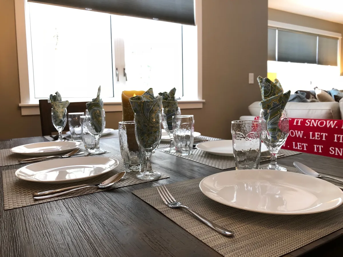 A beautifully set dining table is the centerpiece here, adorned with colorful napkins, glassware, and a decorative centerpiece, evoking a sense of warmth and celebration ideal for family gatherings and memorable meals.