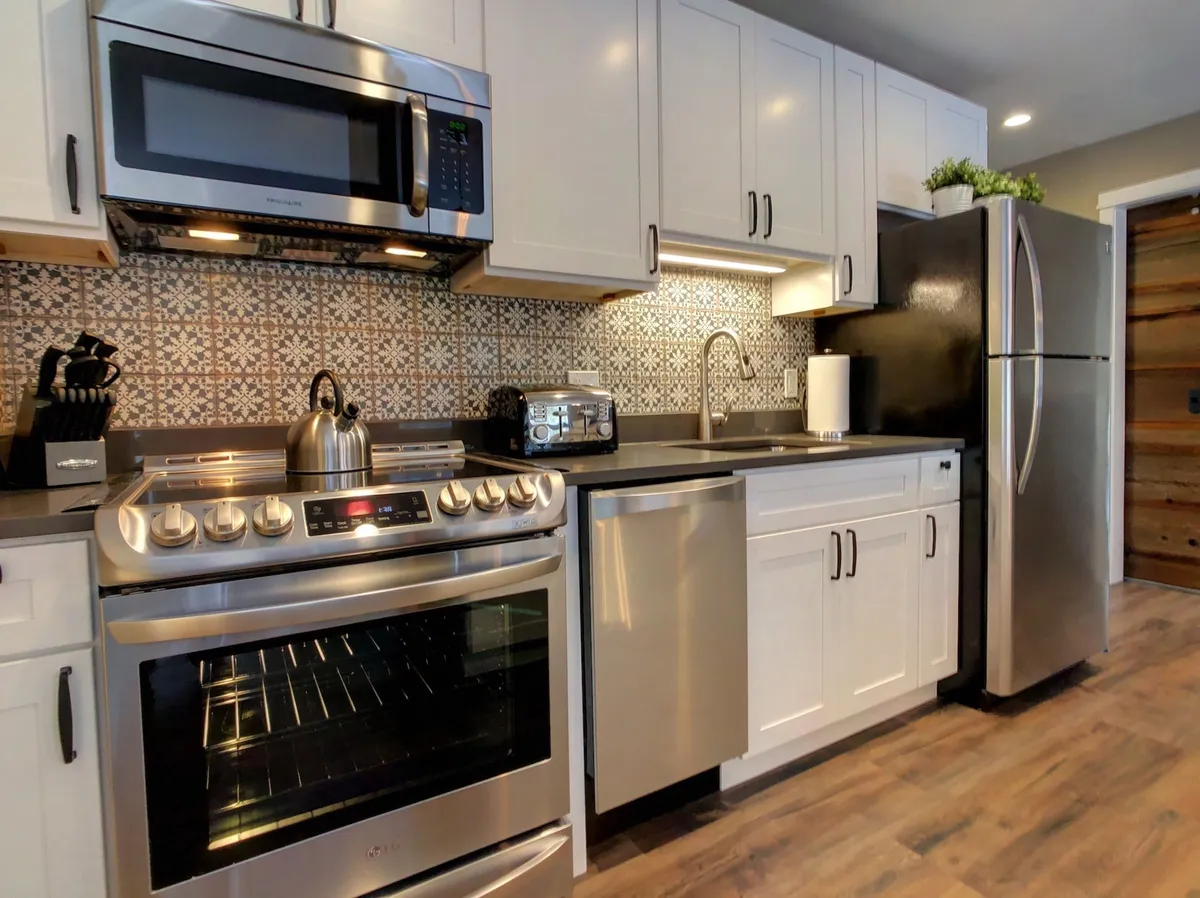 This image presents a close-up view of the modern farmhouse kitchen, highlighting sleek stainless steel appliances, a decorative backsplash, and a kettle on the stove. Warm lighting enhances the inviting atmosphere, perfect for gathering around the kitchen.