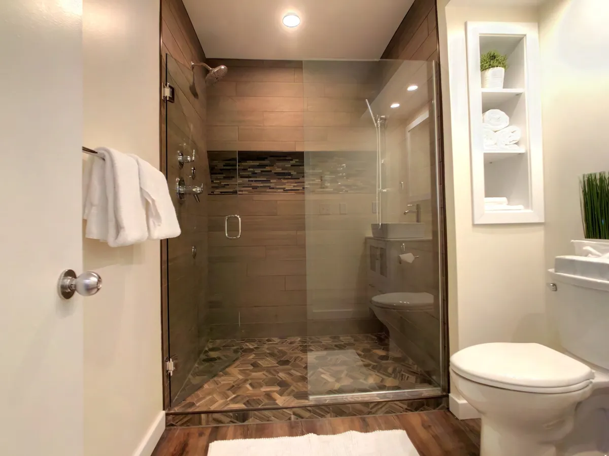 This image features a glass shower enclosure with textured floor tiles and a sleek, wall-mounted storage shelf. The serene, spa-like atmosphere is enhanced by modern finishes and a focus on relaxation and personal care.