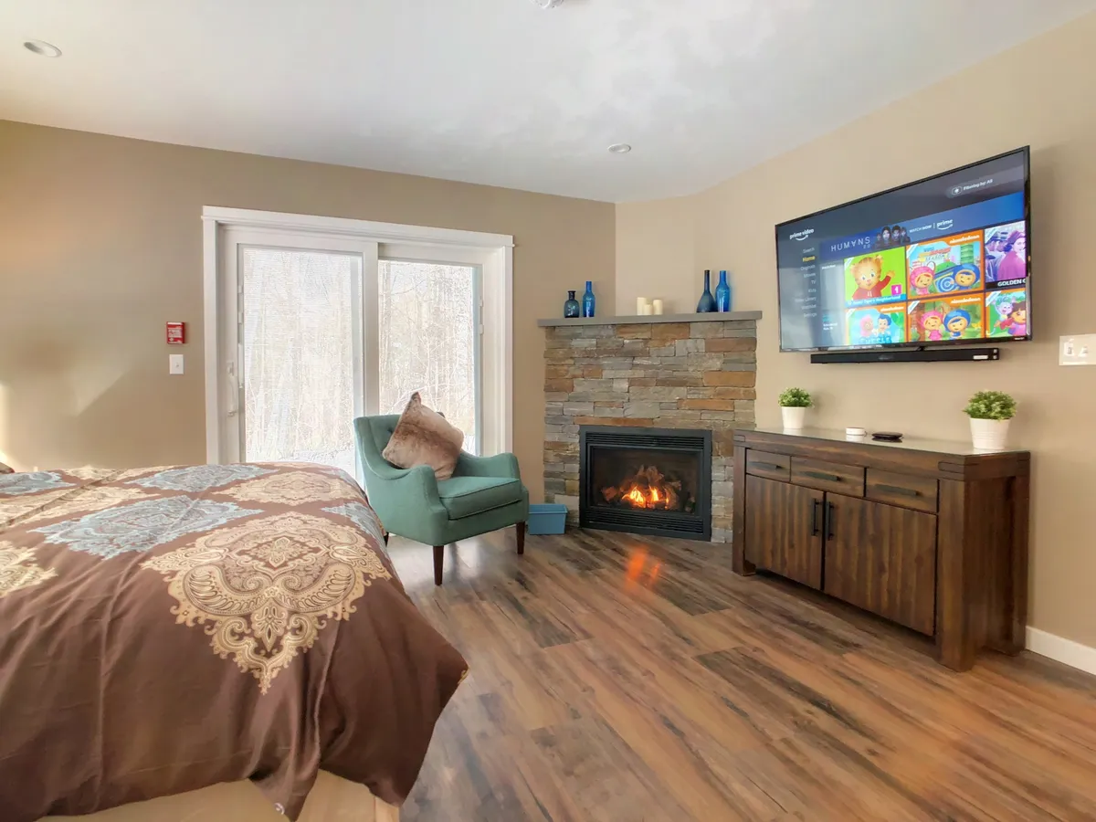 A warm, inviting living area featuring a fireplace, comfortable bed, television, and a cozy chair. The mood is intimate and relaxing, perfect for unwinding after a night out or enjoying a quiet evening indoors.