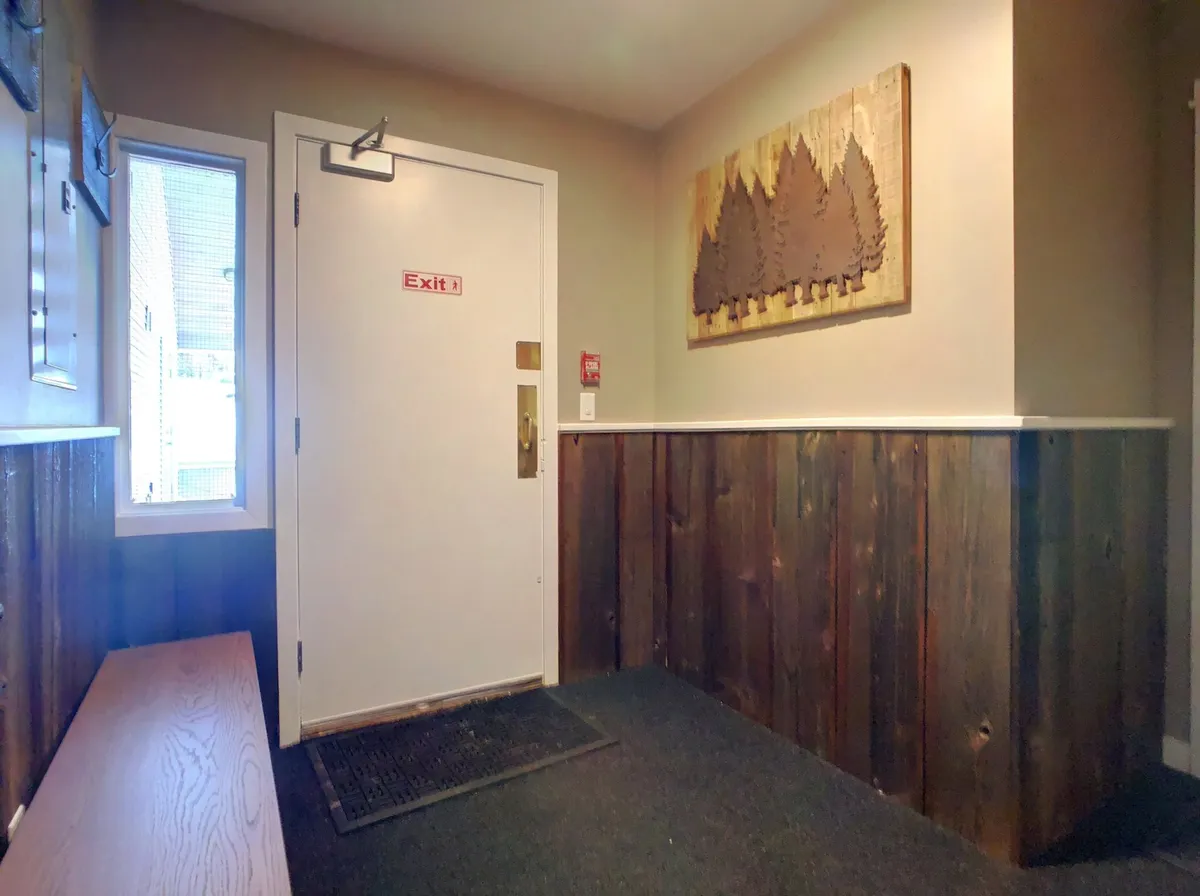 A cozy, inviting shot of the property’s entryway, featuring an exit door, wooden wall art, and a bench. The mood is welcoming, suggesting a transition point between indoor comfort and outdoor adventure.