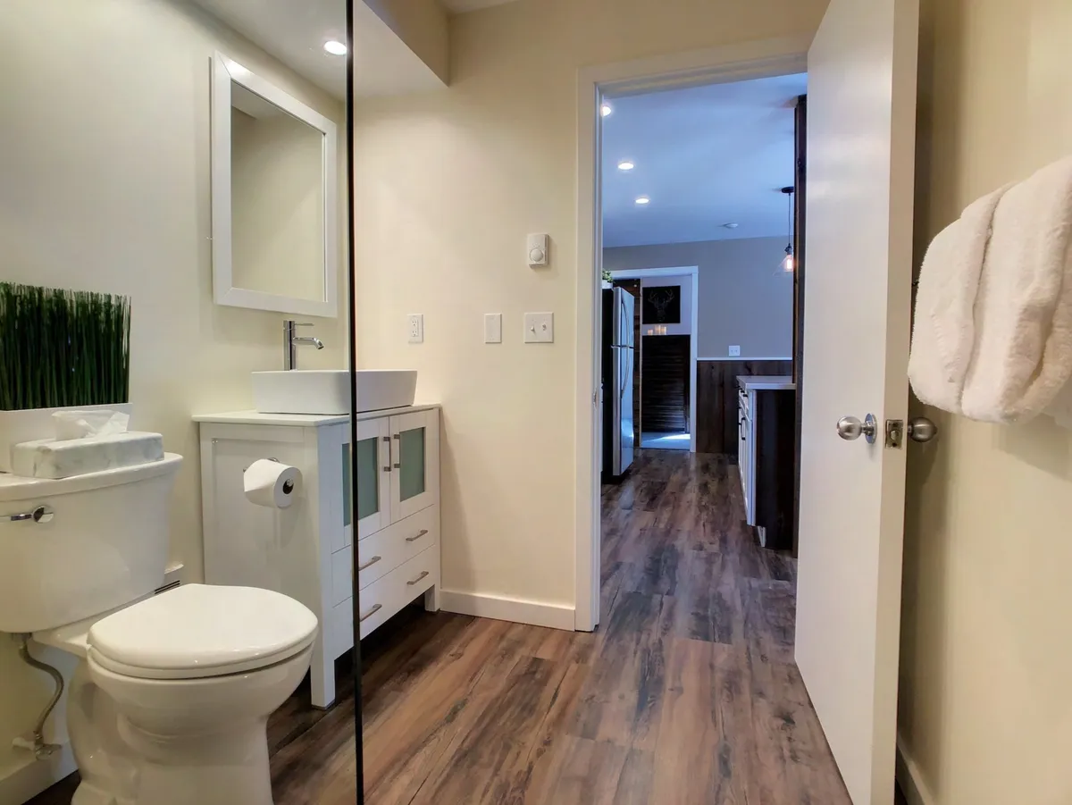 A sleek vanity and bathroom area with a bright mirror, modern sink, and doorway connecting to the kitchen. The space is filled with morning light, offering a refreshing spot for personal grooming before a special occasion.