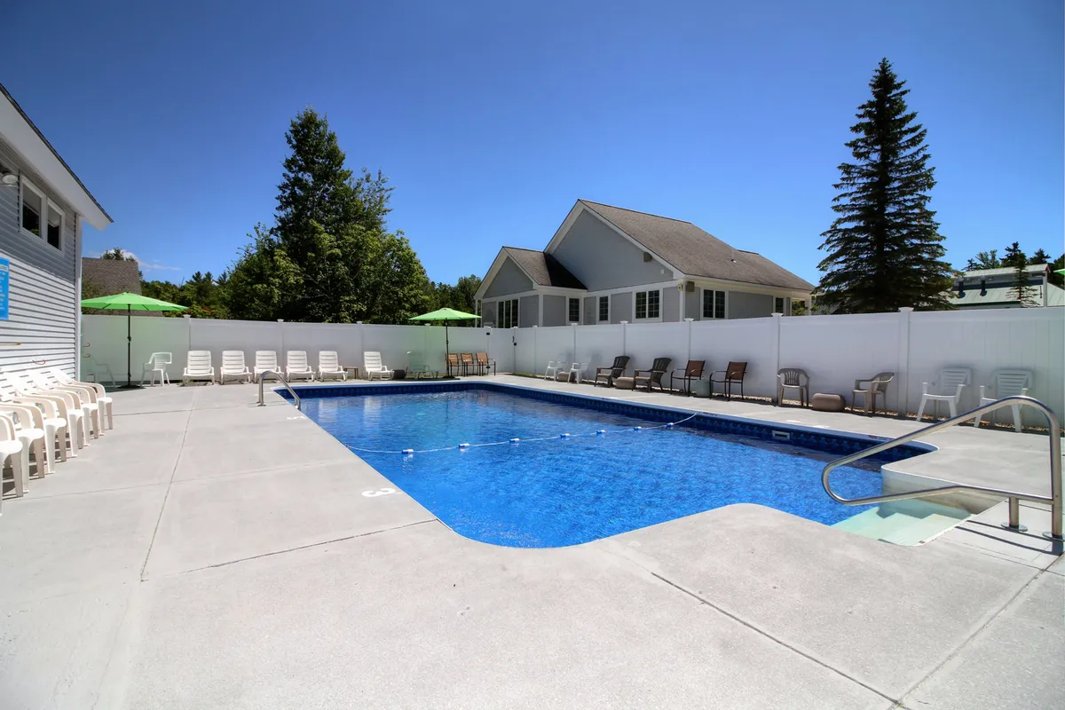 An inviting poolside view featuring a swimming pool with lounge chairs, green umbrellas, and a backdrop of trees. The ambiance is relaxed and perfect for sunbathing, socializing, and unwinding after outdoor activities.