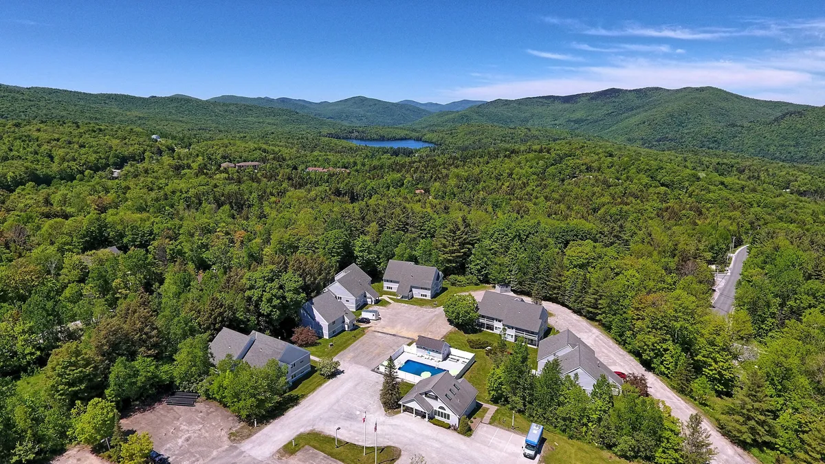This exterior image showcases a sparkling swimming pool surrounded by lush trees and the backdrop of Vermont's beautiful mountains. The area is inviting, with plenty of space for lounging and enjoying the outdoors. The pool is central in the frame, emphasizing its appeal for both relaxation and active family fun.