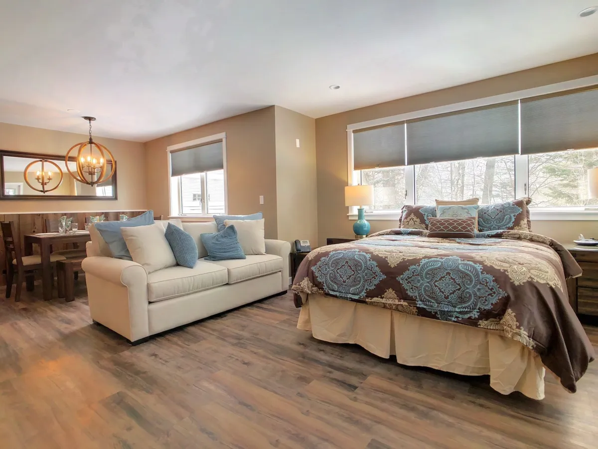 A multi-functional living area with a comfortable sofa, a bed, a dining table, and a chandelier. The arrangement suggests both communal gathering and additional sleeping options, reflecting the section’s note that the living room doubles as sleeping space for larger groups.